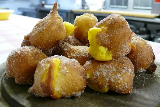 Frittelle di Carnevale ancora calde, spolverate di zucchero, su un tagliere di legno.