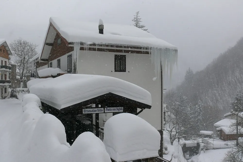 La Locanda sepolta dalla neve, con lunghi ghiaccioli dal tetto e il cartello all'ingresso che annuncia crescentine fritte e pasta con fagioli.