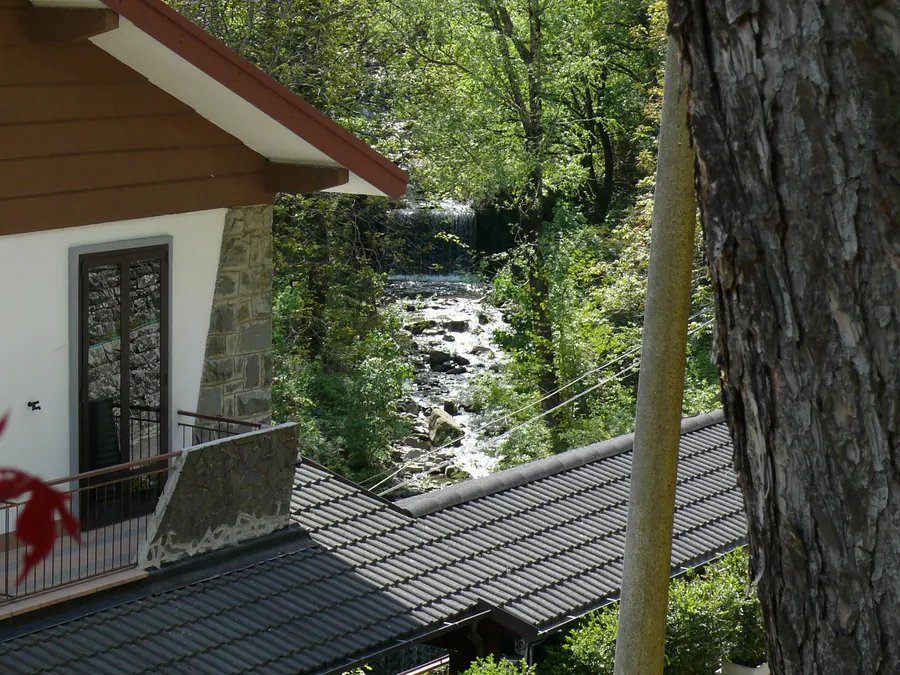 Dal terrazzo della Locanda: il rio che scende fra i sassi con un piccolo salto d'acqua, i tetti del paese e il bosco.