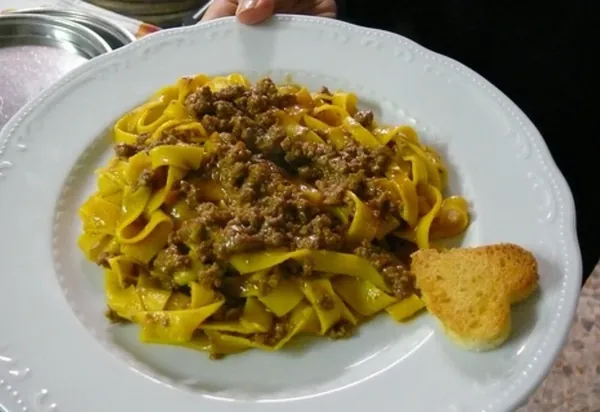 Tagliatelle al ragù con un crostino di pane a forma di cuore sul bordo del piatto.