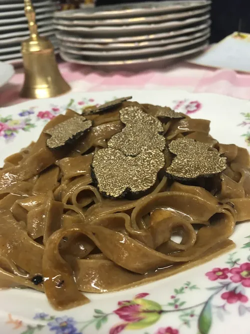 Le tagliatelle scure di Pianaccio, servite su un piatto a fiori con lamelle di tartufo nero.