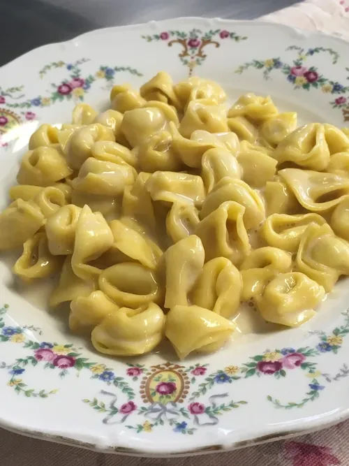 Tortellini in crema di parmigiano su un piatto di ceramica a fiori.